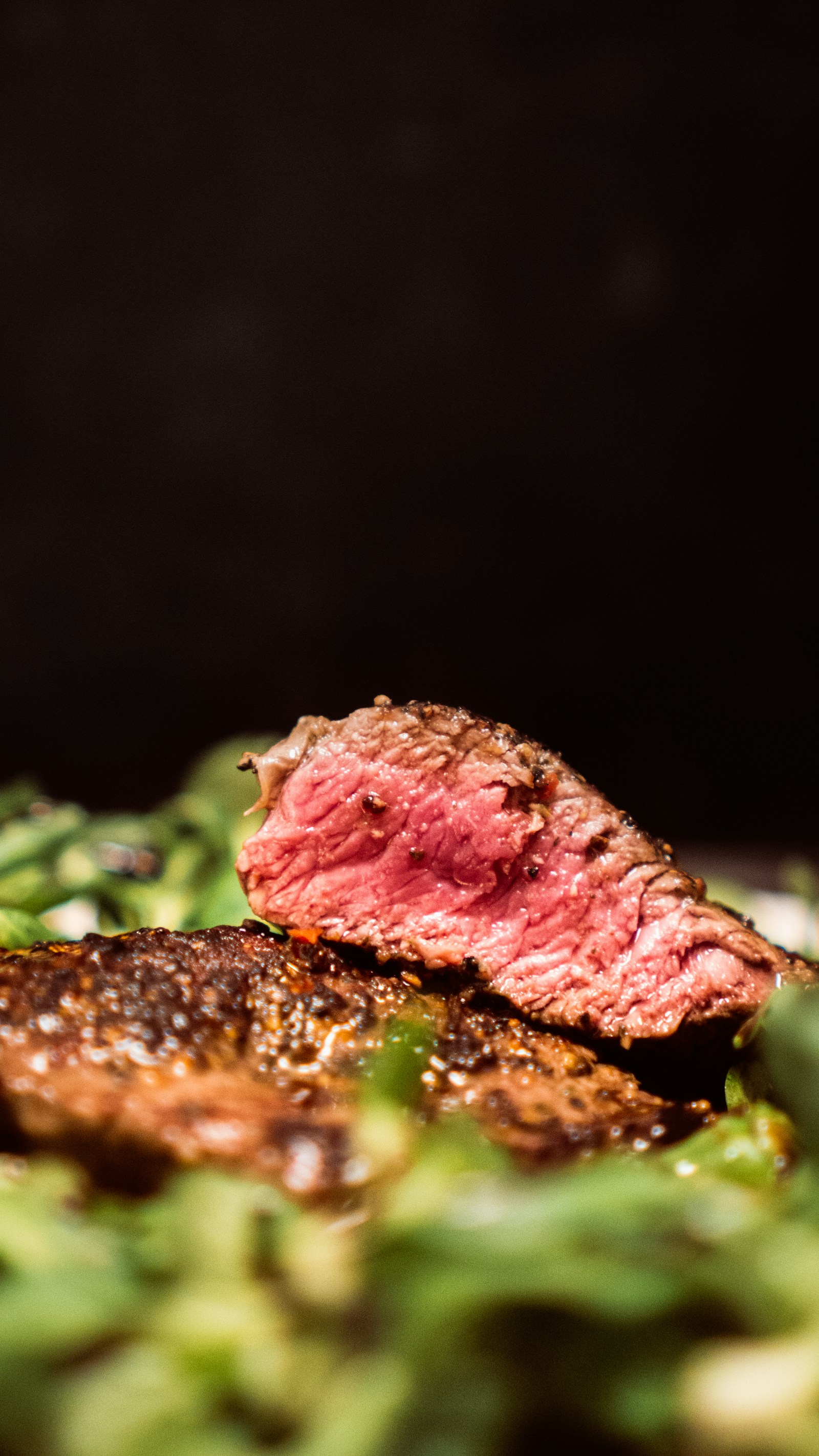 Seared steak with a pink center resting on fresh salad leaves