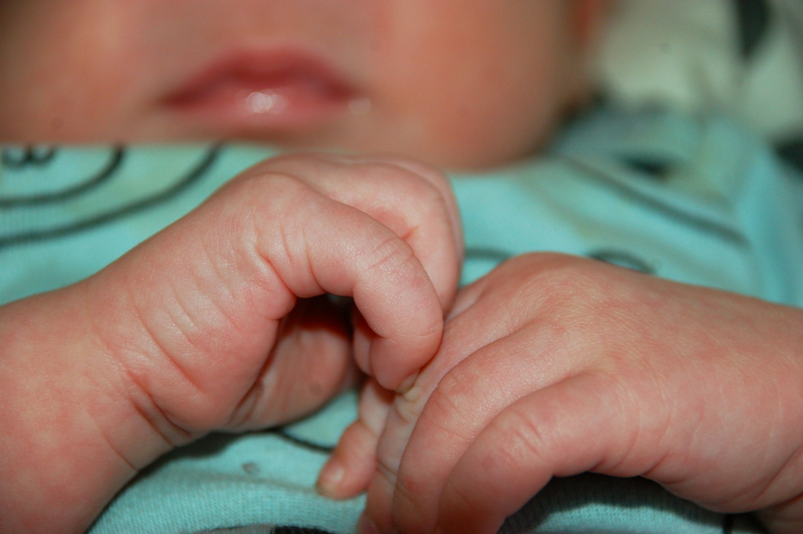 A baby's hand resting on a soft blue blanket